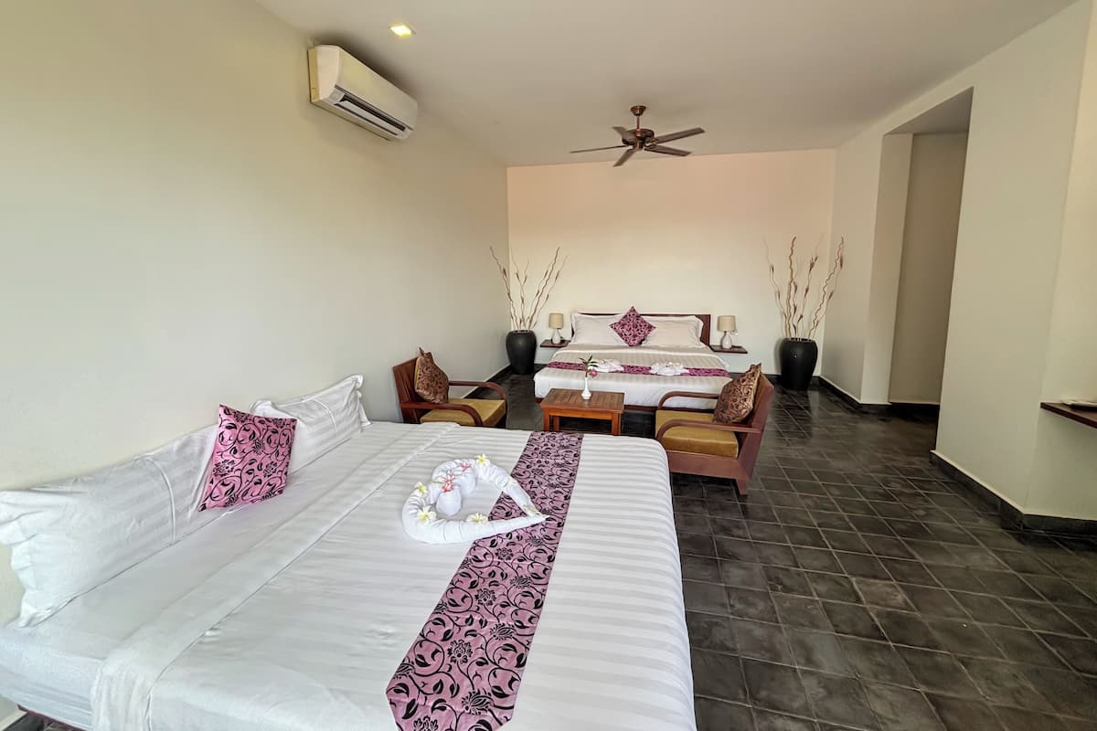 A hotel room with two beds, a ceiling fan, and a large potted plant.