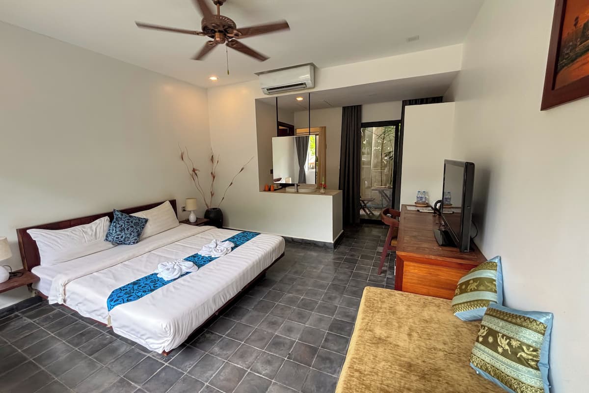 A hotel room with a bed, a desk, a television, and a ceiling fan.