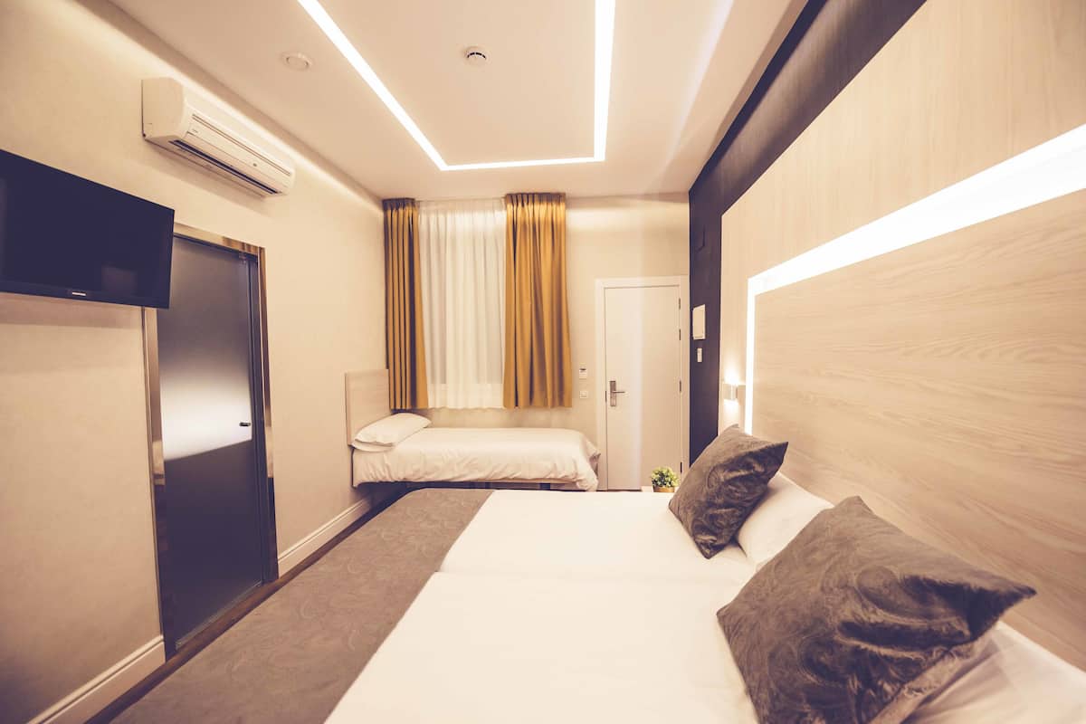A hotel room with a large bed, a smaller bed, a TV, an air conditioner, and a door.