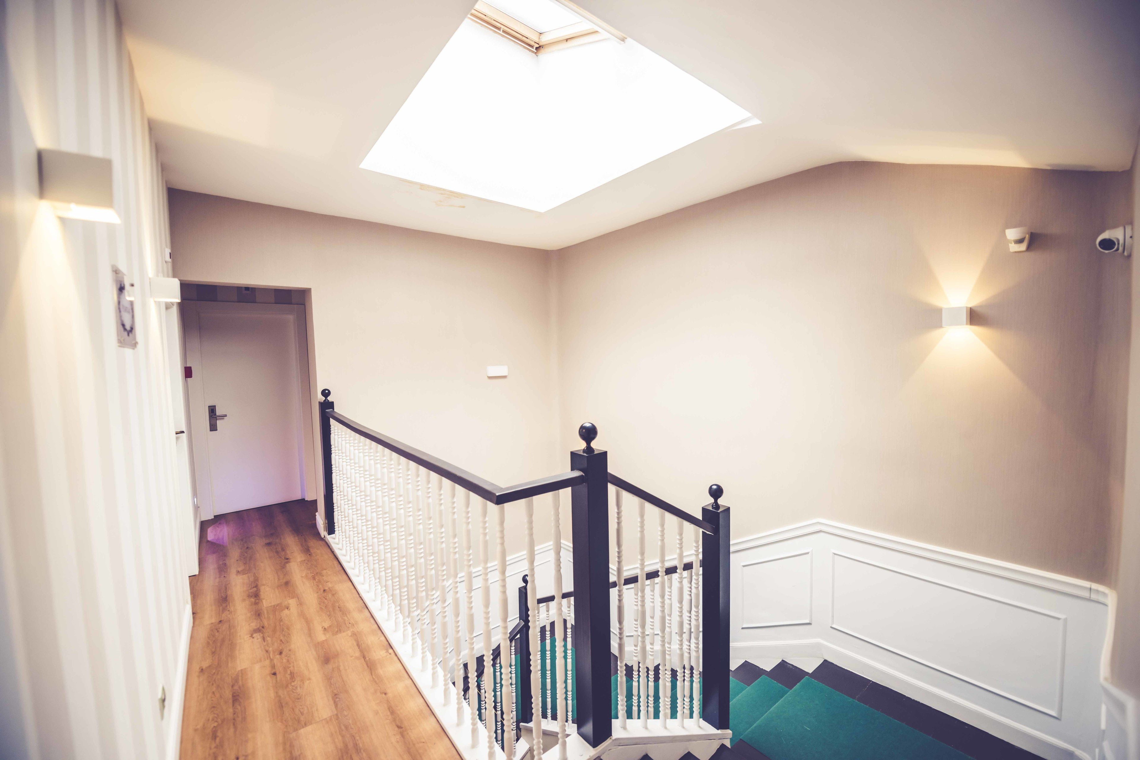 A staircase with a skylight, wooden flooring, and a white wall with a light switch.