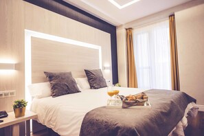 A modern hotel room with a neatly made bed, a tray with croissants and orange juice, and a small potted plant on the nightstand. - Hostal Lisboa (Madrid)