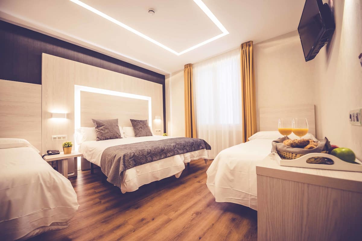 A hotel room with two beds, a bedside table with a lamp, a flat-screen TV mounted on the wall, and a breakfast tray on the nightstand.