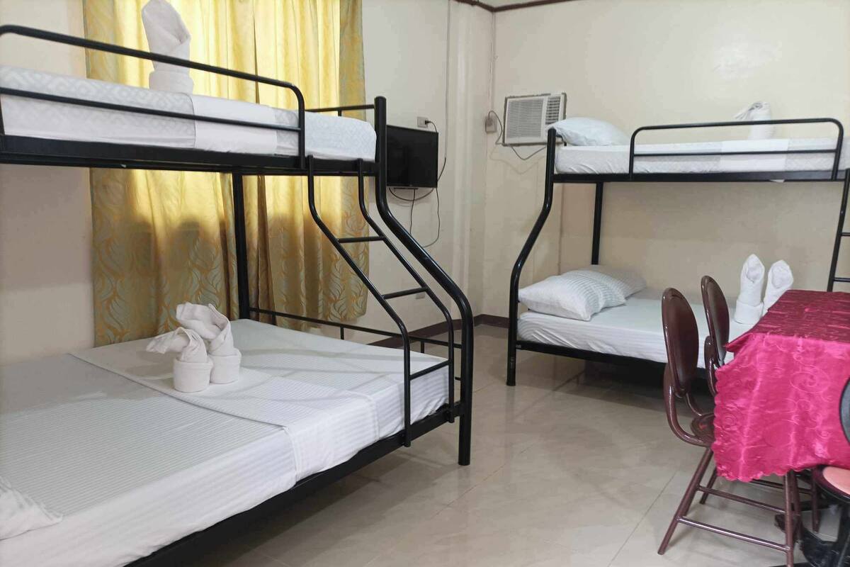 A room with two bunk beds, a table with a pink tablecloth, and a chair.