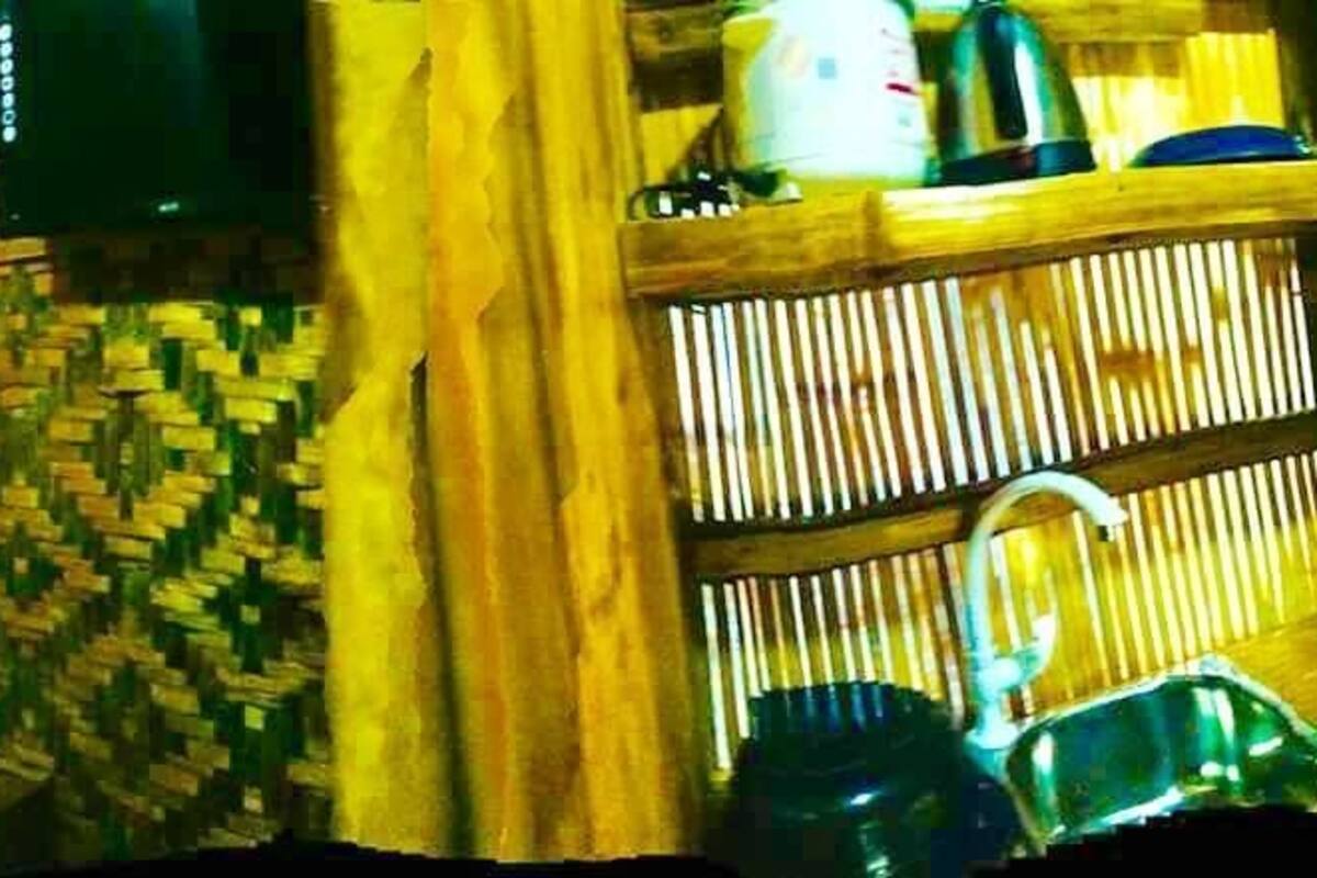 A room with a bed covered in a blue sheet, a wooden wall with a woven pattern, and a shelf with various items.