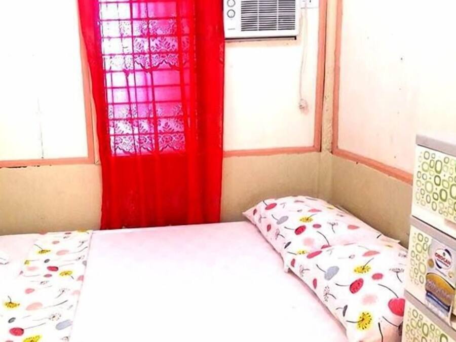 Una habitación pequeña con cama individual, ventana, calefacción y mesita de noche con lámpara.