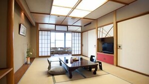 Una habitación japonesa tradicional con suelo de tatami, una mesa baja, puertas correderas y un televisor.