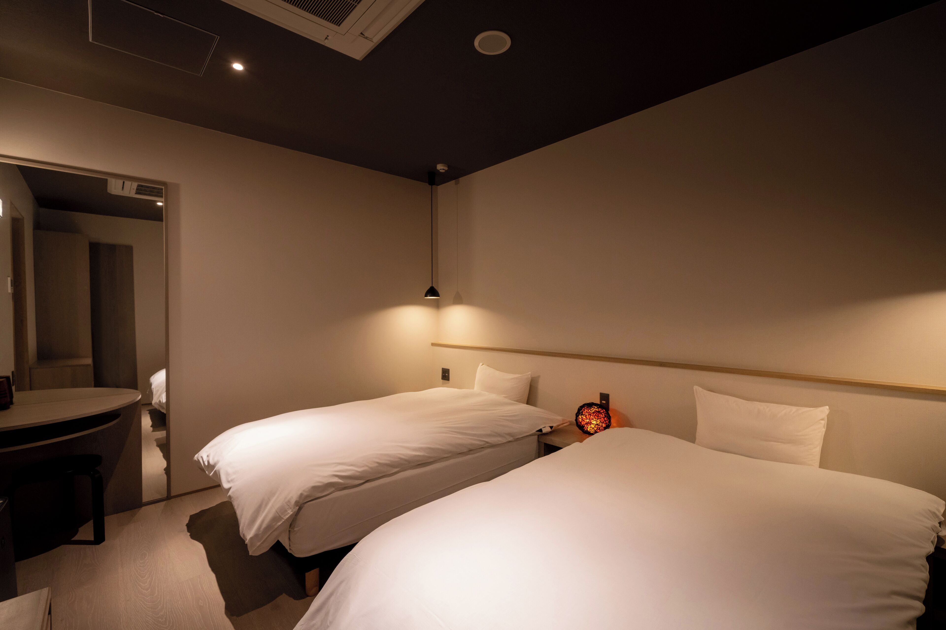 A hotel room with two single beds, a desk, and a chair.