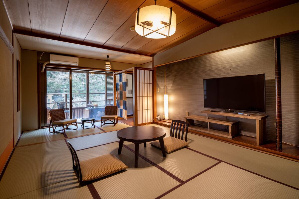 Une pièce de style japonais traditionnel, avec un sol recouvert de tatamis, une télévision et une porte coulissante donnant sur un balcon.