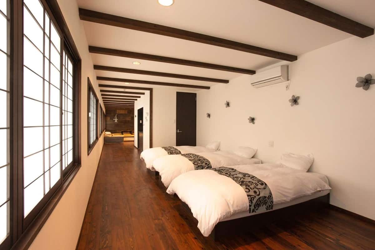 Une chambre d’hôtel avec un long couloir, un plancher en bois, de grandes fenêtres et un lit recouvert d’une literie à motifs.
