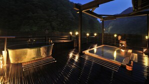 Um deck de madeira com hidromassagem e sauna, cercado por uma cerca de madeira e com montanhas ao fundo.