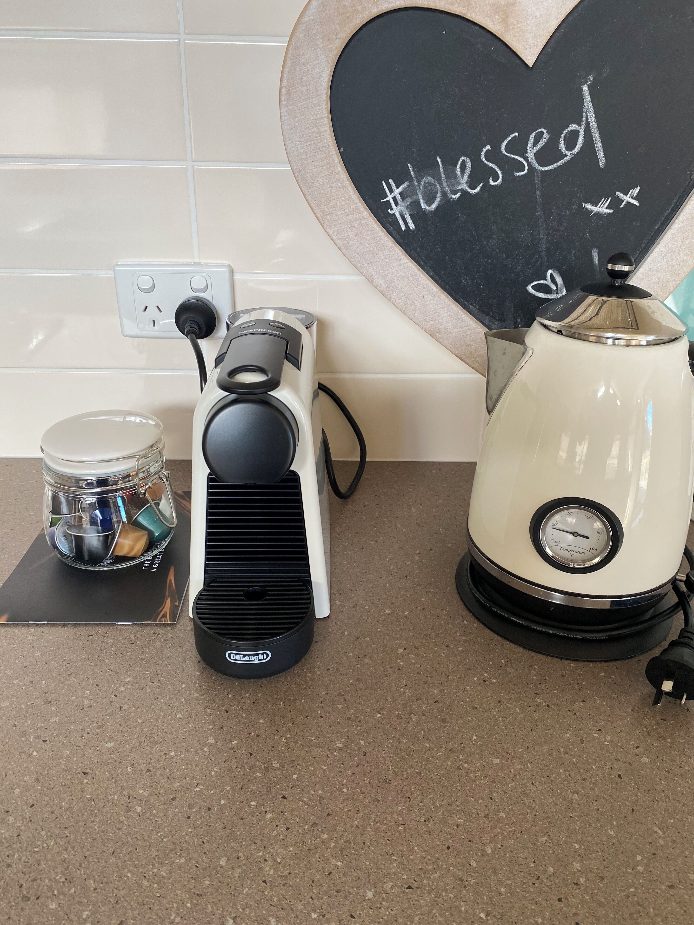 Une cuisine équipée d’une machine à café, d’un bocal de thé et d’un tableau noir sur lequel est écrit le mot « béni ».