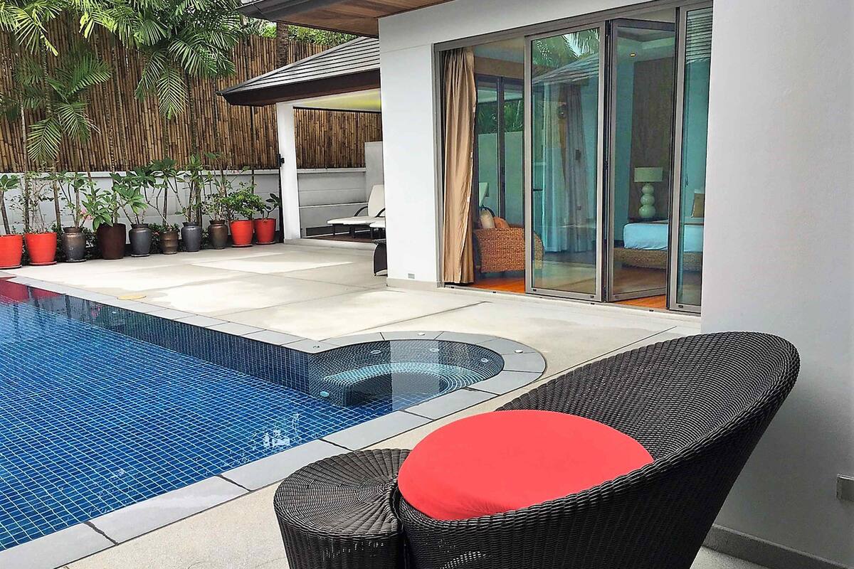 A modern outdoor pool area with a glass-enclosed hot tub, wicker furniture, and potted plants.