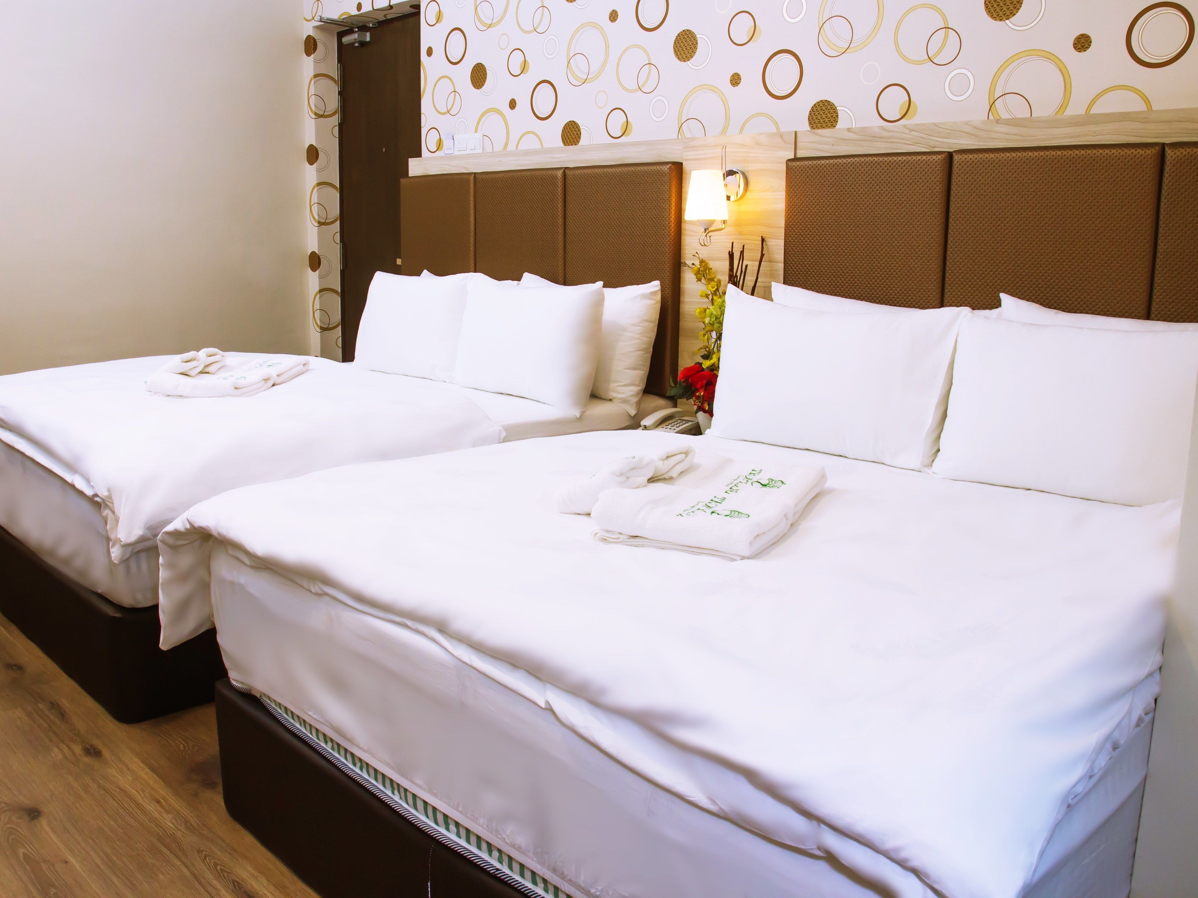 A hotel room with two beds, each with white linens and towels. There is a wall-mounted lamp and a telephone on the nightstand.