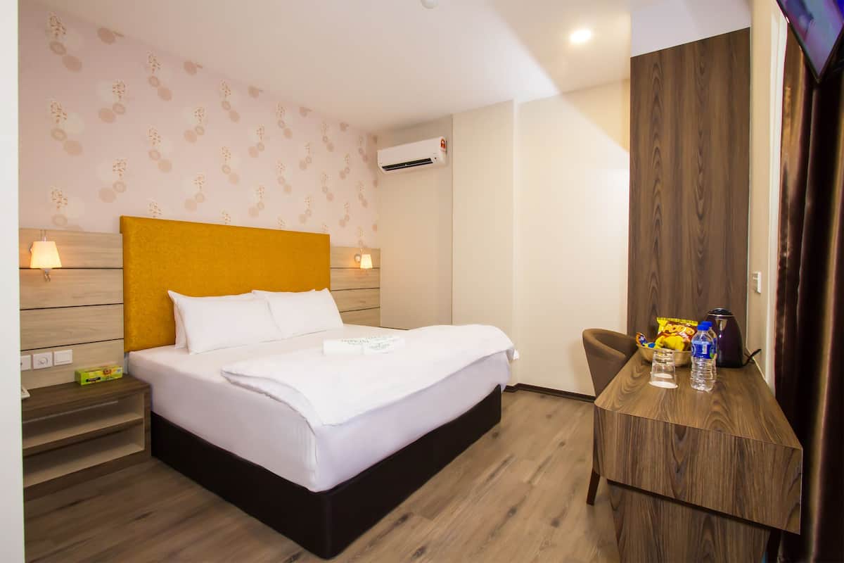 A hotel room with a bed, bedside table, and a small desk with a chair.