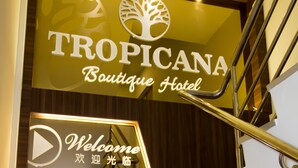 Una escalera conduce al Hotel Boutique Tropicana, con un letrero de 'Bienvenido' y un símbolo de botón de reproducción.