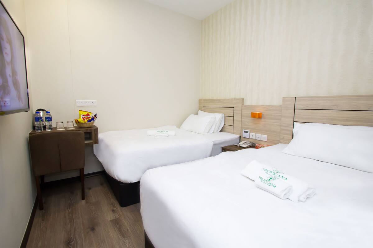 A hotel room with two beds, a wooden nightstand, a small table, and a wall-mounted TV.