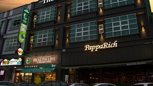 Un edificio con varios letreros, incluyendo 'TROPICANA Boutique Hotel' y 'PappaRich'.