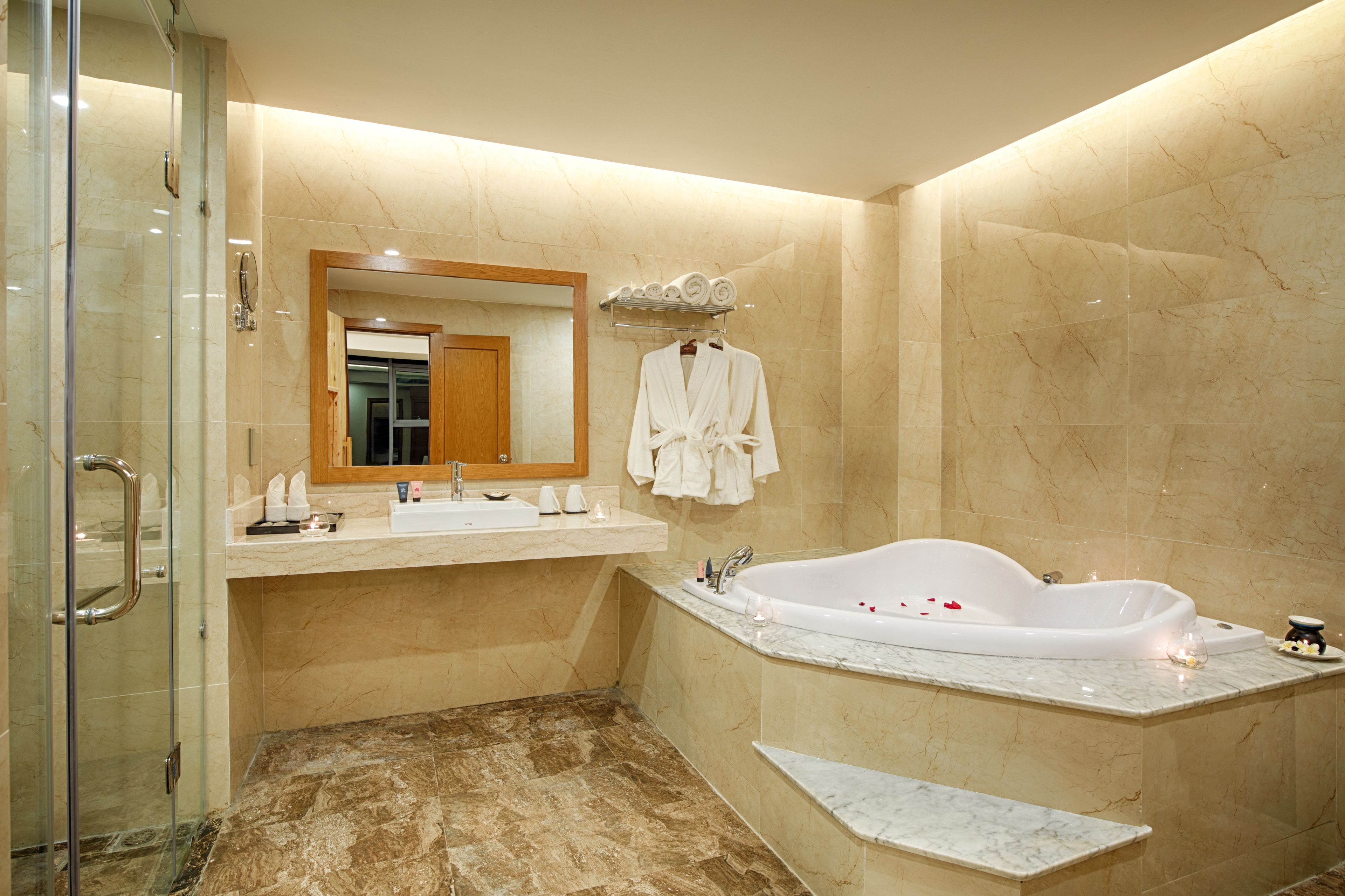 A modern bathroom with a glass shower enclosure, a large bathtub, and marble walls.