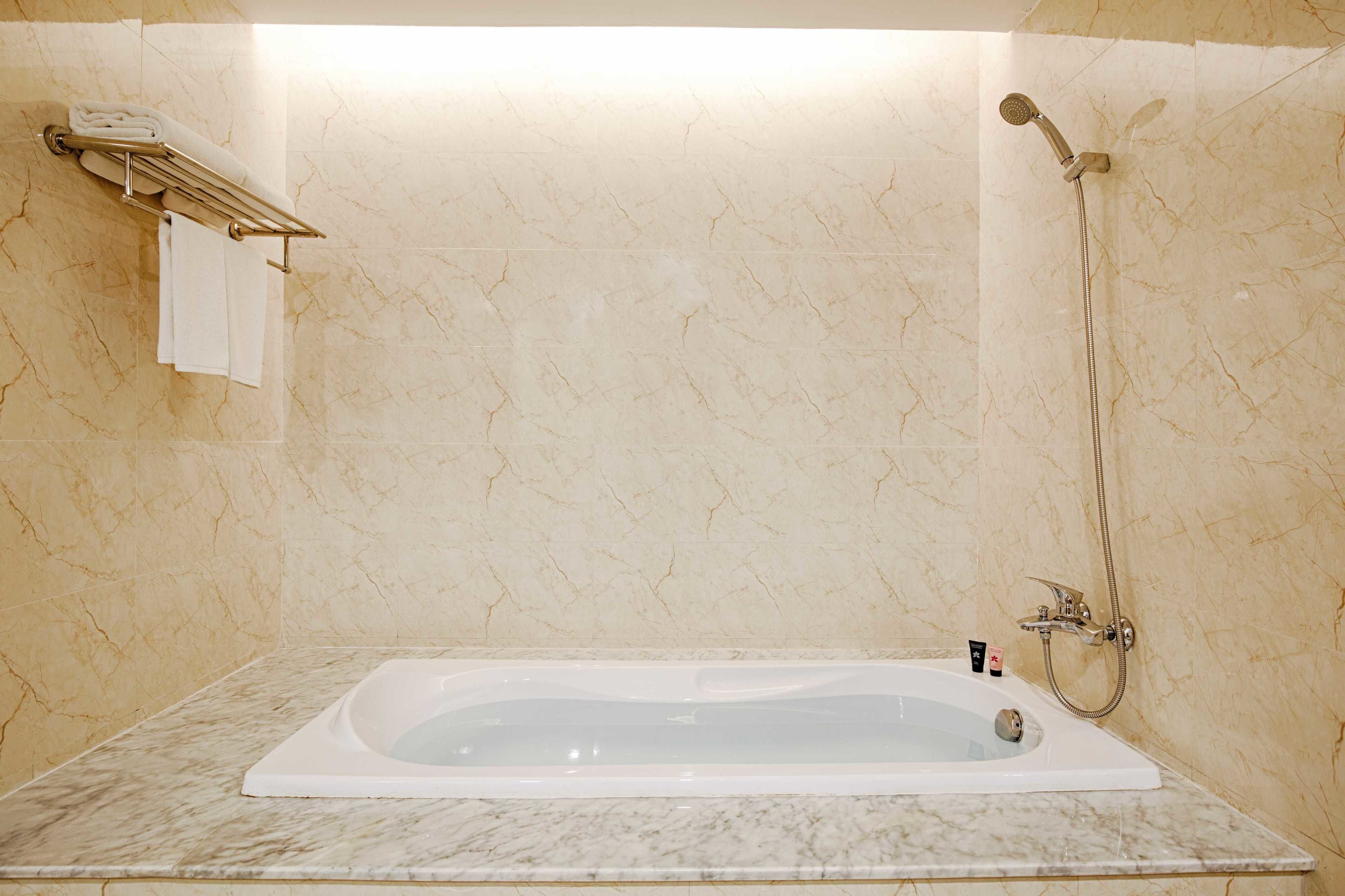 A bathroom with a marble-tiled wall, a white bathtub, a towel rack with folded towels, and a handheld showerhead.