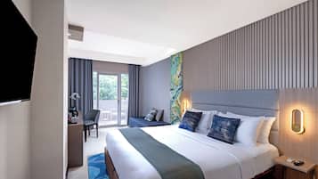 A modern hotel room with a large bed, a desk with a chair, and a view of the outdoors through a sliding door.