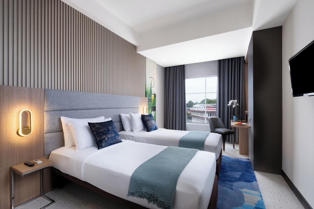 Ett hotellrum med två sängar, ett skrivbord, en stol, en TV och ett fönster med utsikt.