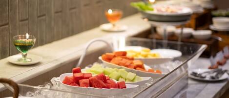 A buffet with various fruits and a candle on the counter.