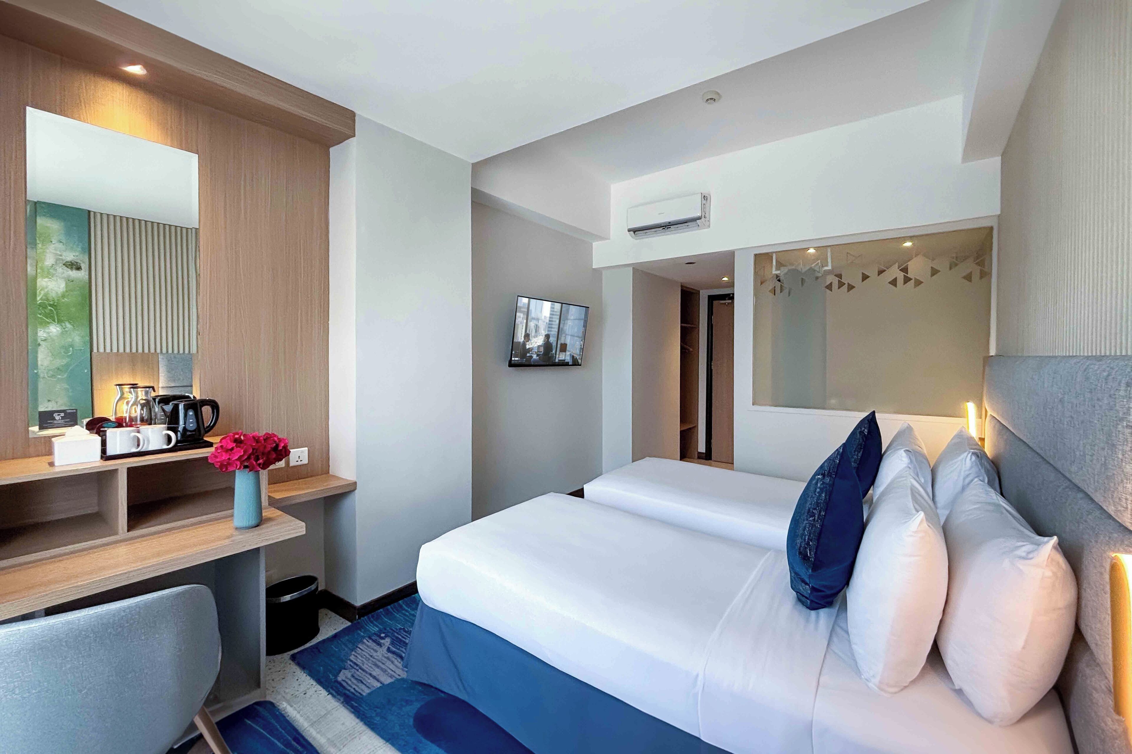 A hotel room with a bed, a desk, a chair, a TV, and an air conditioning unit.