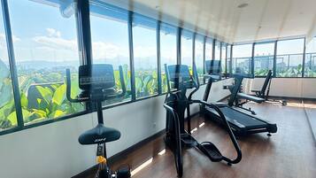 A gym with exercise equipment and large windows offering a view of greenery and mountains.