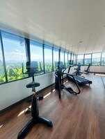 Une salle de sport équipée de matériel d’exercice et dotée de grandes fenêtres offrant une vue sur la verdure et les montagnes.