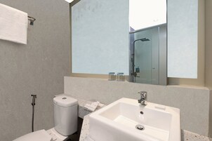 Uma casa de banho moderna com um espelho grande, uma sanita branca e uma loiça de lavatório.