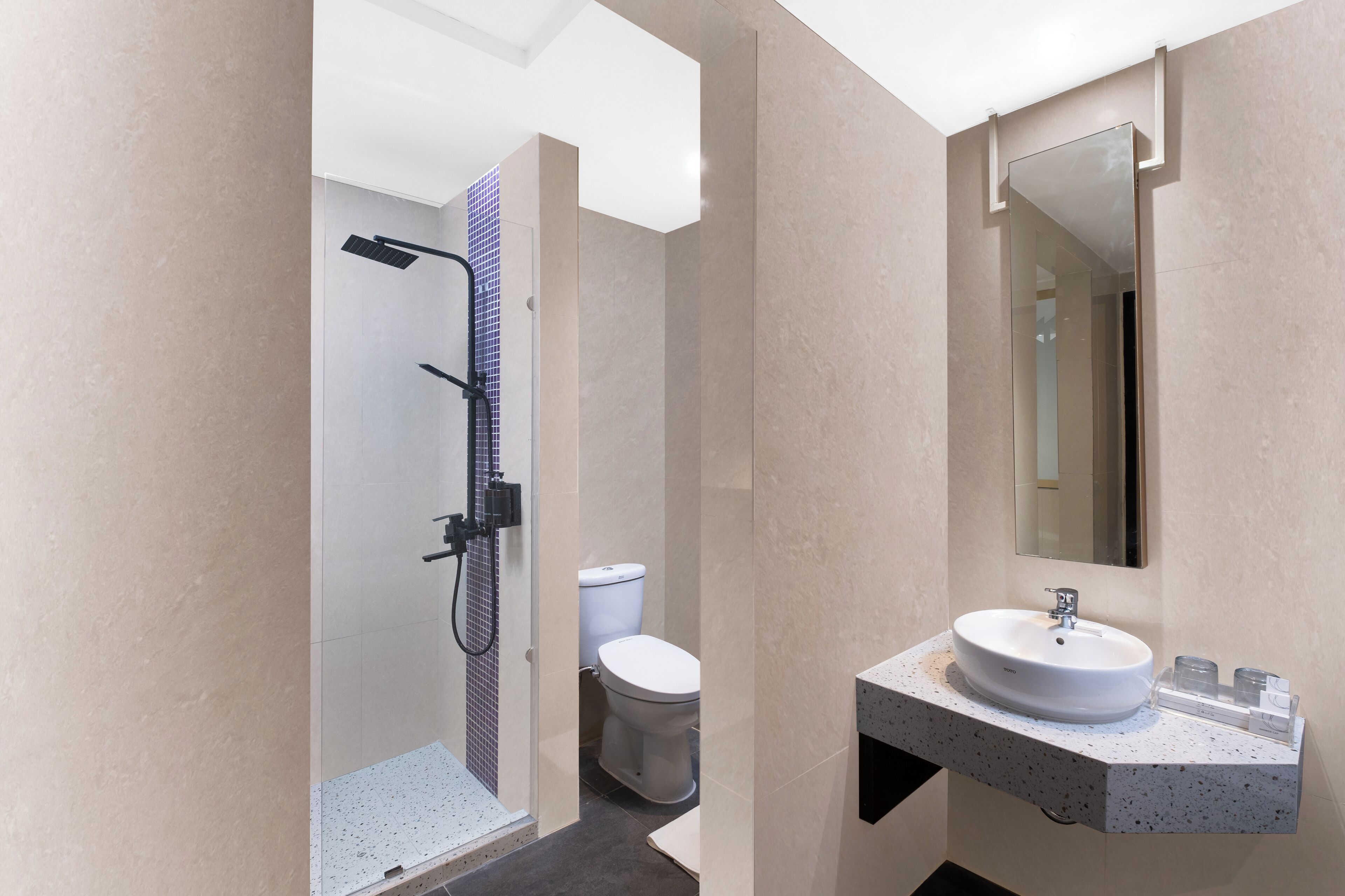 Een moderne badkamer met een glazen douchecabine, een witte wastafel met een marmeren aanrechtblad en een grote spiegel boven de wastafel.