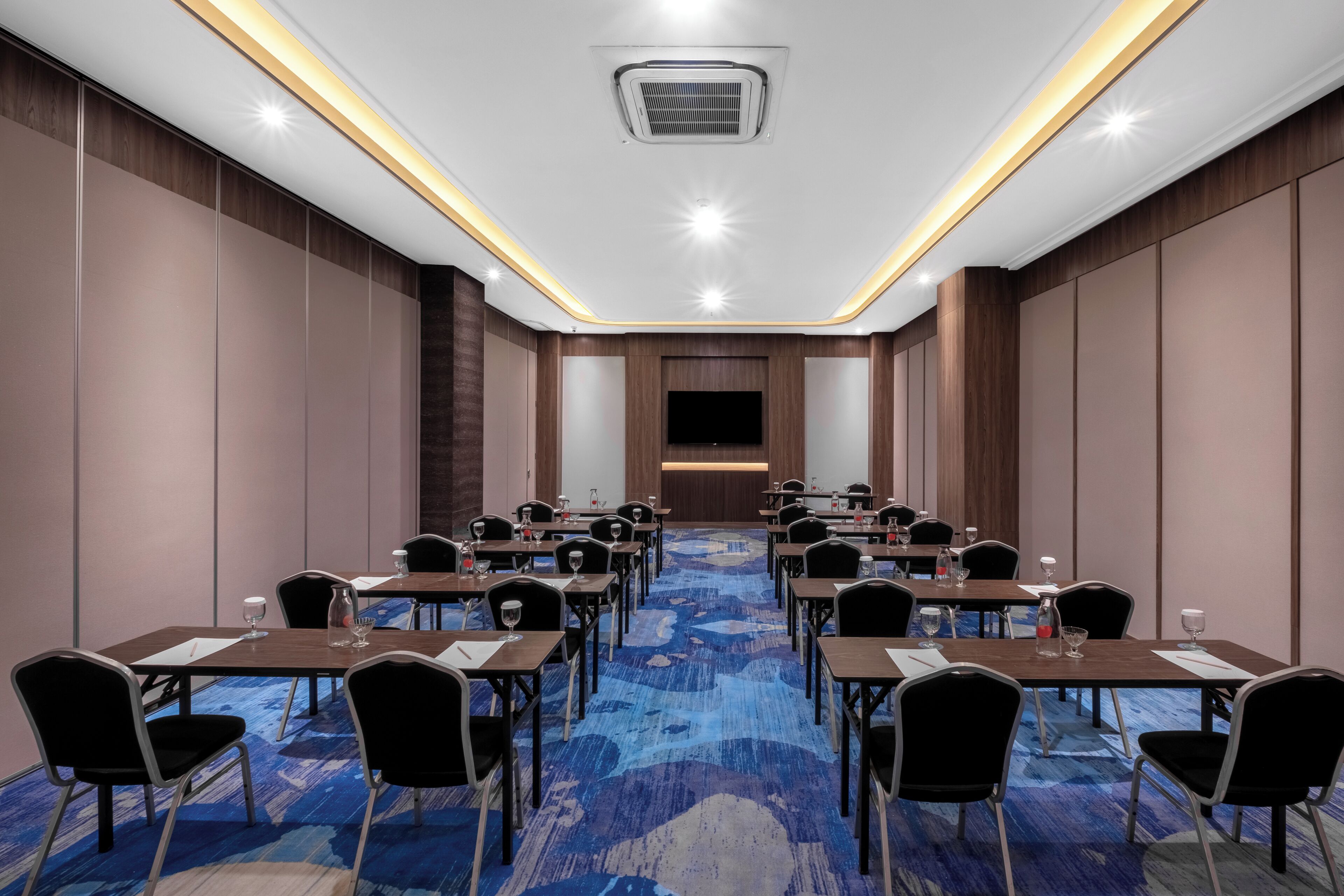 A conference room with a blue carpet, wooden panel walls, and a flat-screen TV at the front.