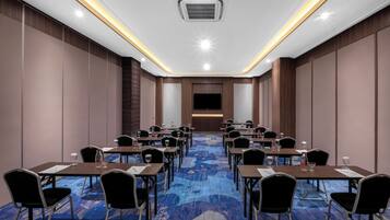 A conference room with a blue carpet, wooden panel walls, and a flat-screen TV at the front.