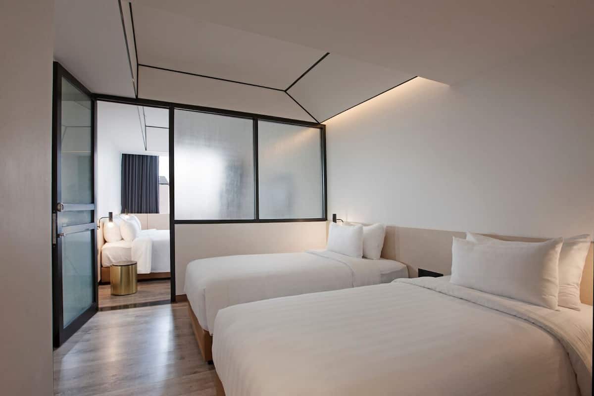 A modern hotel room with two single beds, a glass partition, and a large window.
