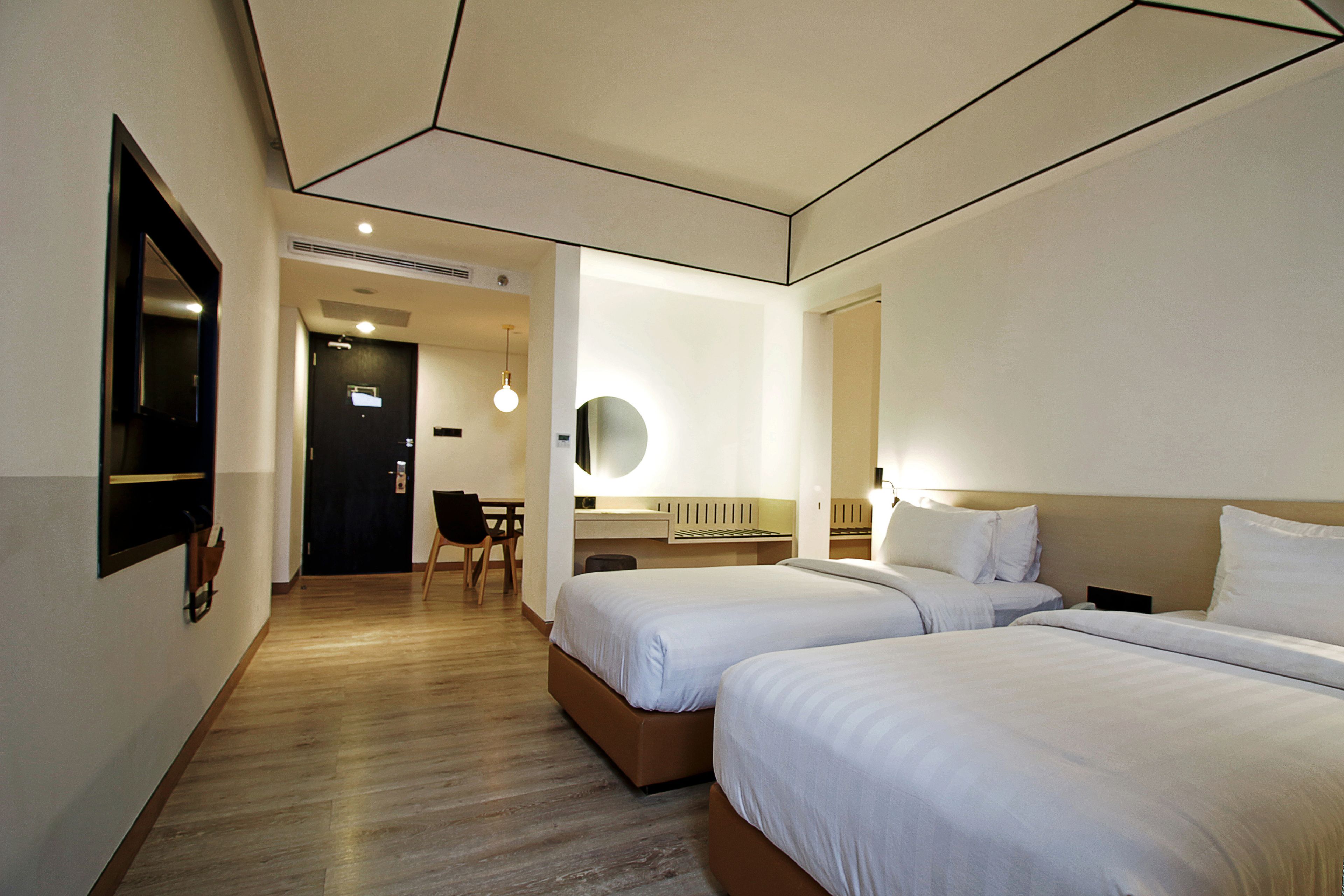 A hotel room with two beds, a desk, a chair, and a mirror.