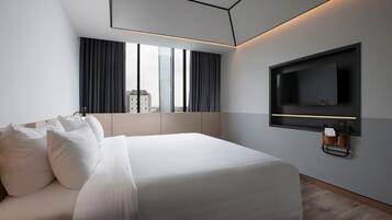 A modern hotel room with a large bed, a flat-screen TV mounted on the wall, and a city view through the window.