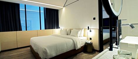 Habitación de hotel moderna con una cama grande, un baño con espejo y vistas a la ciudad por la ventana.