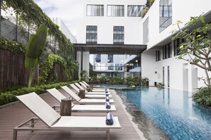 A modern hotel with a pool, lounge chairs, and a wooden deck. - Gaia Cosmo Hotel (Yogyakarta)