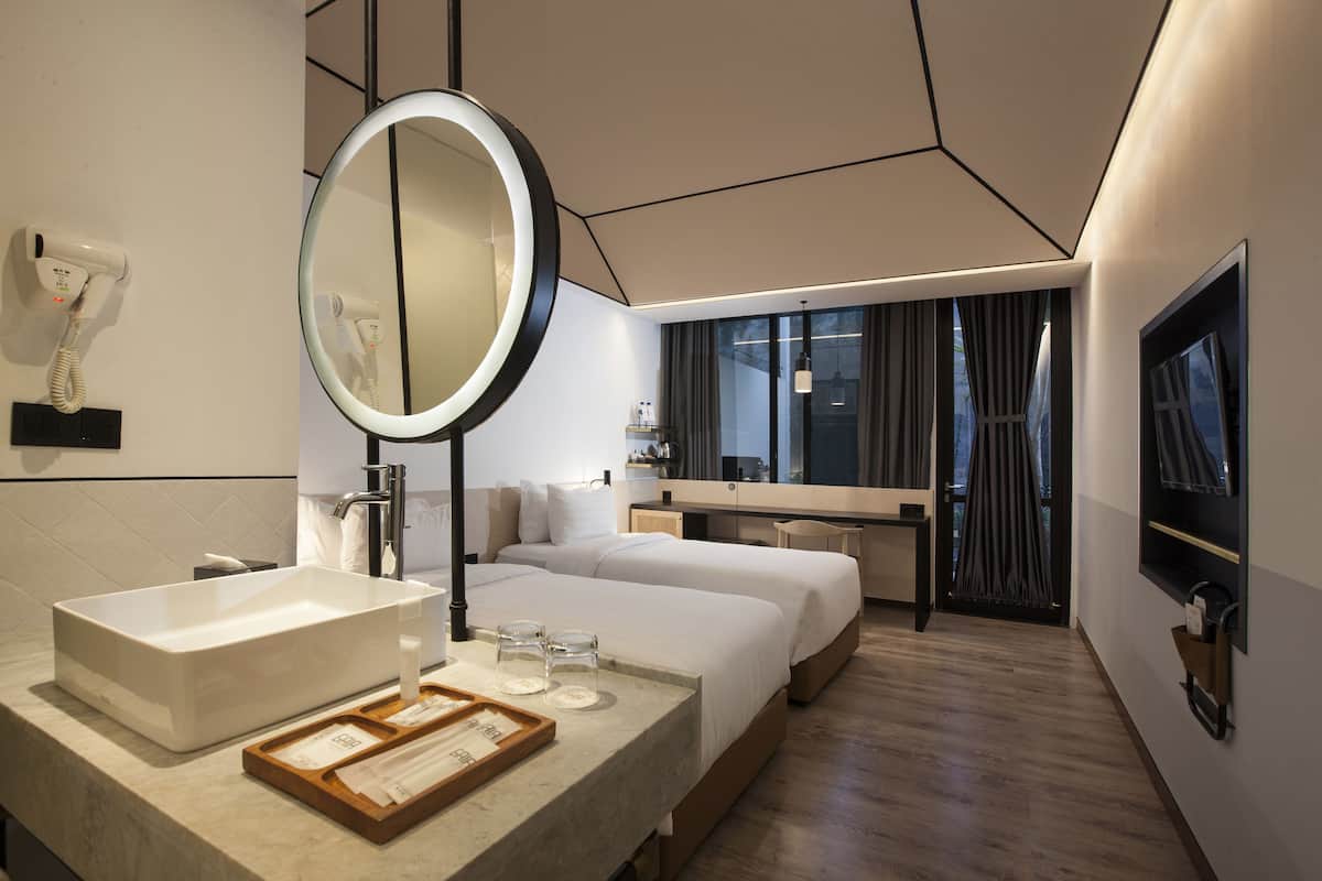 A modern hotel room with a large mirror, a bedside table with a tray, a large window, and a flat-screen TV mounted on the wall.
