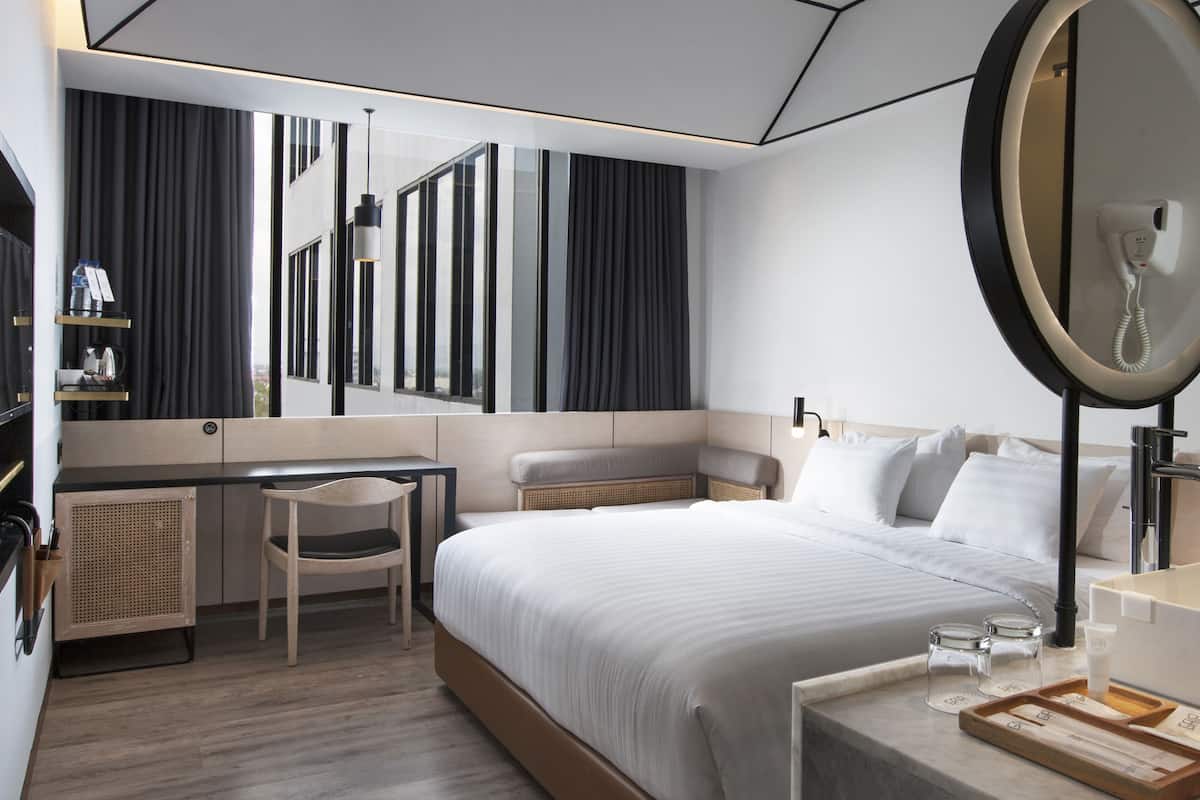 A modern hotel room with a large bed, a desk, a chair, a mirror, and a small table with toiletries.