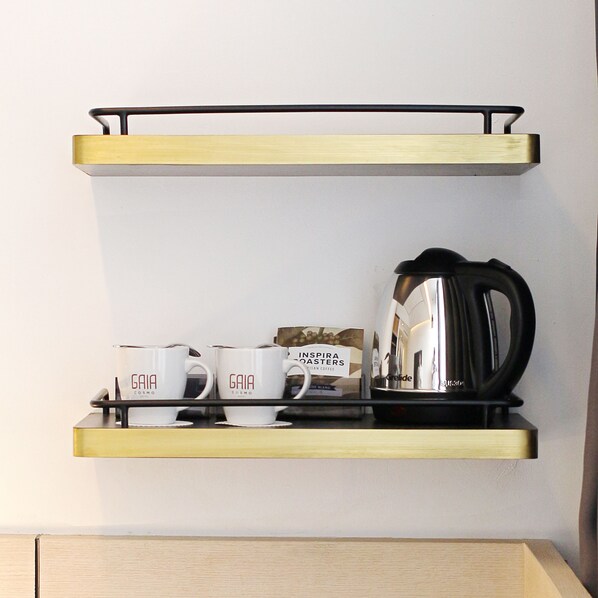 A kitchen area with two black hanging shelves, one above the other, holding a coffee maker and three white cups with the brand "GAIA COSMO" on them.