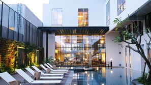 A modern building with a glass facade, a swimming pool, and lounge chairs.