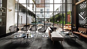 Un área de estar interior moderna con mesas y sillas redondas, y grandes ventanales que ofrecen vistas del exterior del edificio.