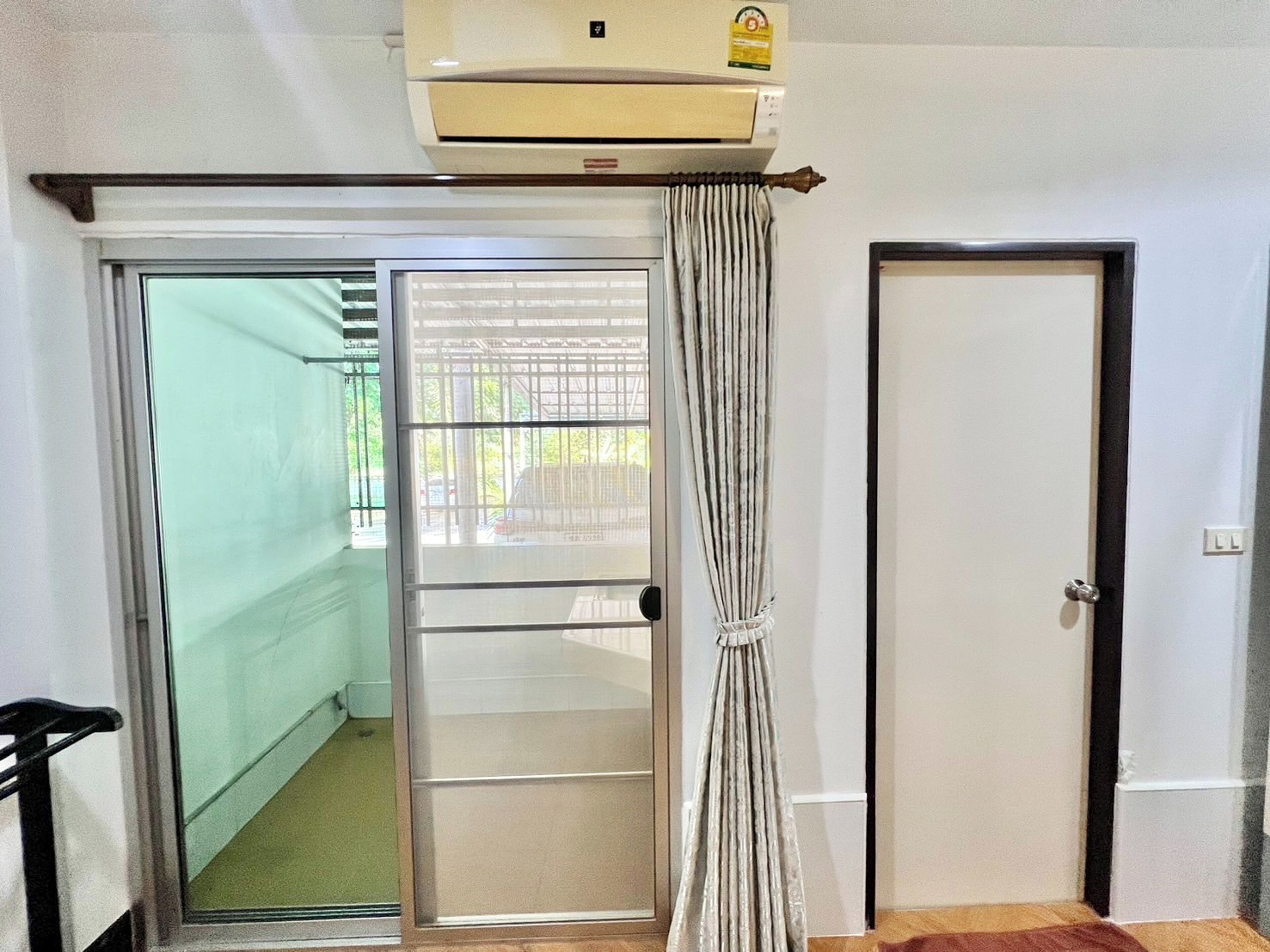 Une pièce dotée d’une porte-fenêtre coulissante donnant sur un balcon, d’une porte classique et d’un appareil de climatisation placé au-dessus de la porte.