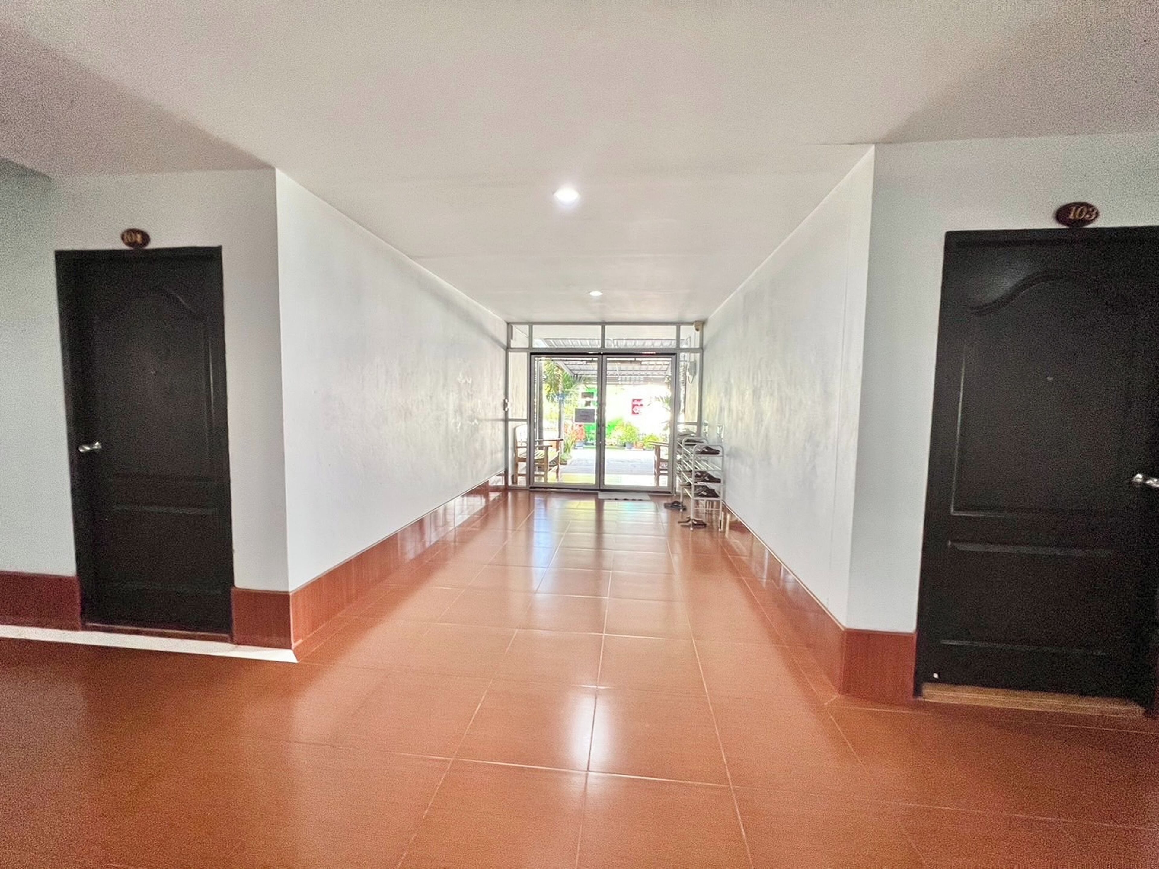 A hallway with a tiled floor, two black doors, and a glass entrance leading outside.