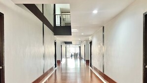 A long, narrow hallway with tiled flooring and white walls, leading to a bright area with a view of the outdoors. - Ban Ton Resort (Udon Thani)