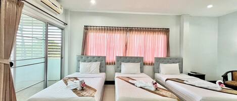A hotel room with three single beds, a large window with blinds, an air conditioning unit, and a view of the outside.