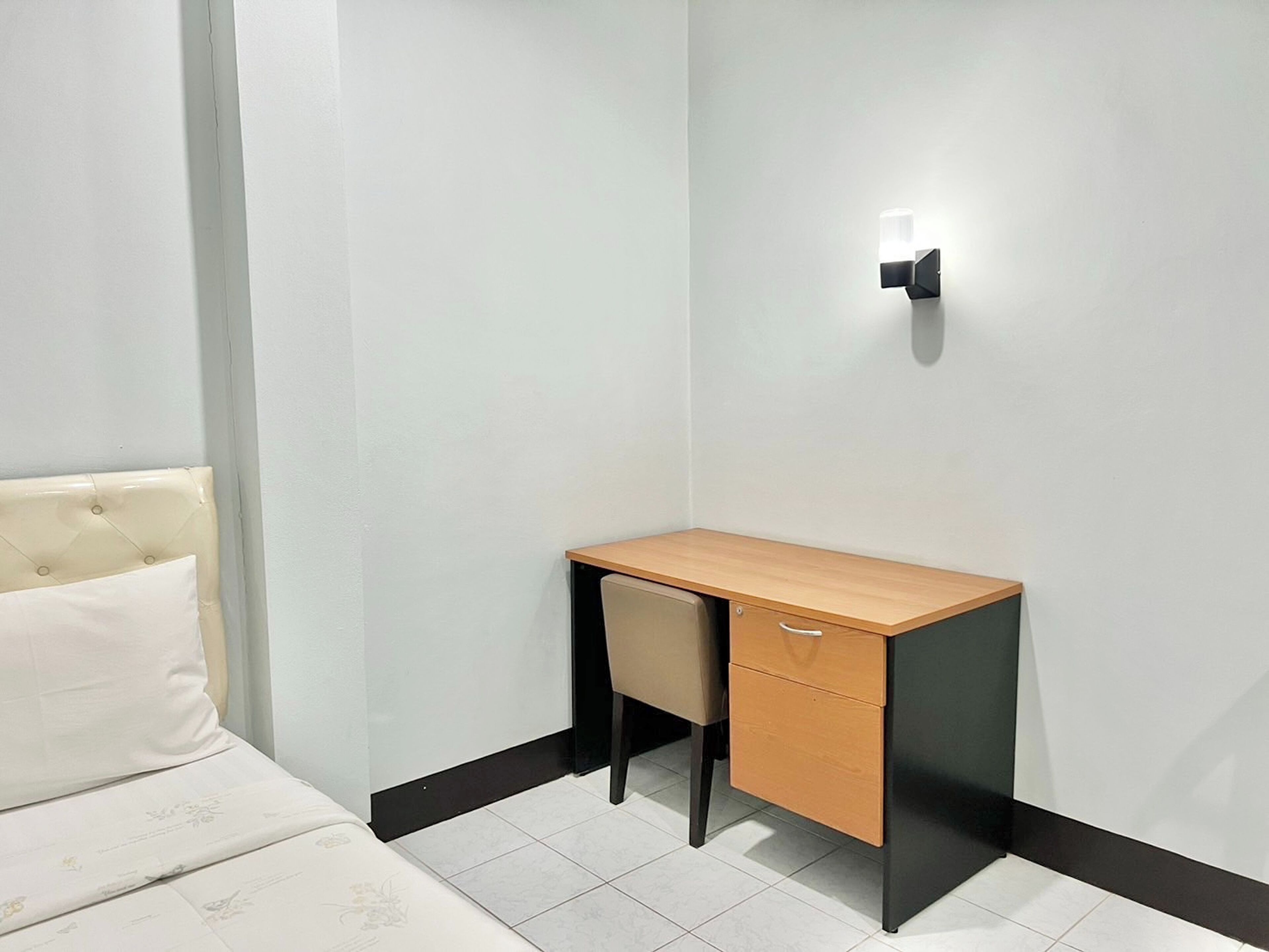 A small, neatly arranged room with a bed, a desk, and a chair.