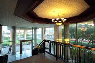 A spacious interior with a high ceiling, large windows, and a staircase with a black railing.