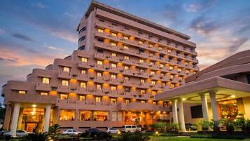 Um hotel de vários andares com design moderno, com varandas em cada piso e uma entrada bem iluminada.